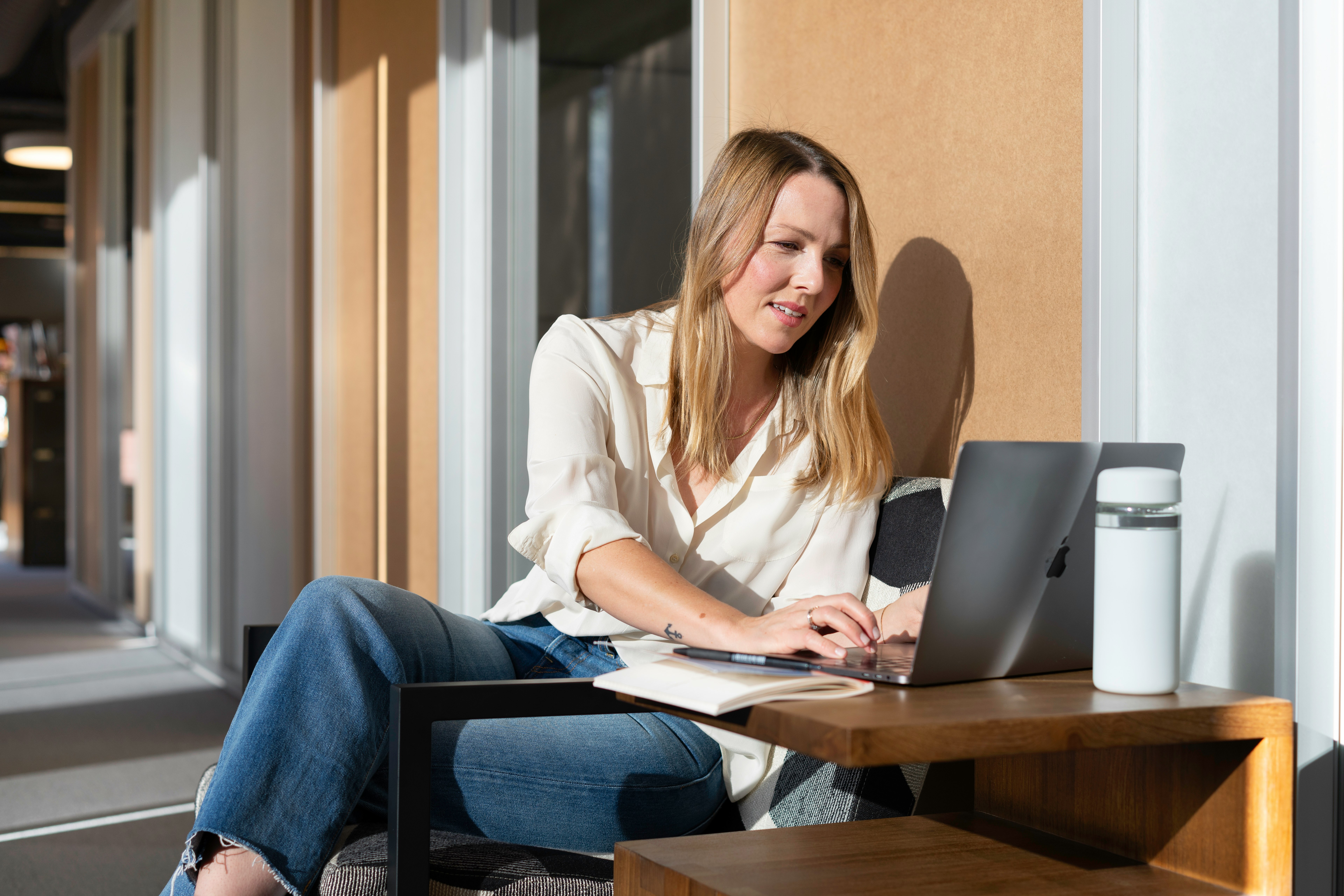 woman in white long sleeve shirt and blue denim jeans sitting on brown wooden table using